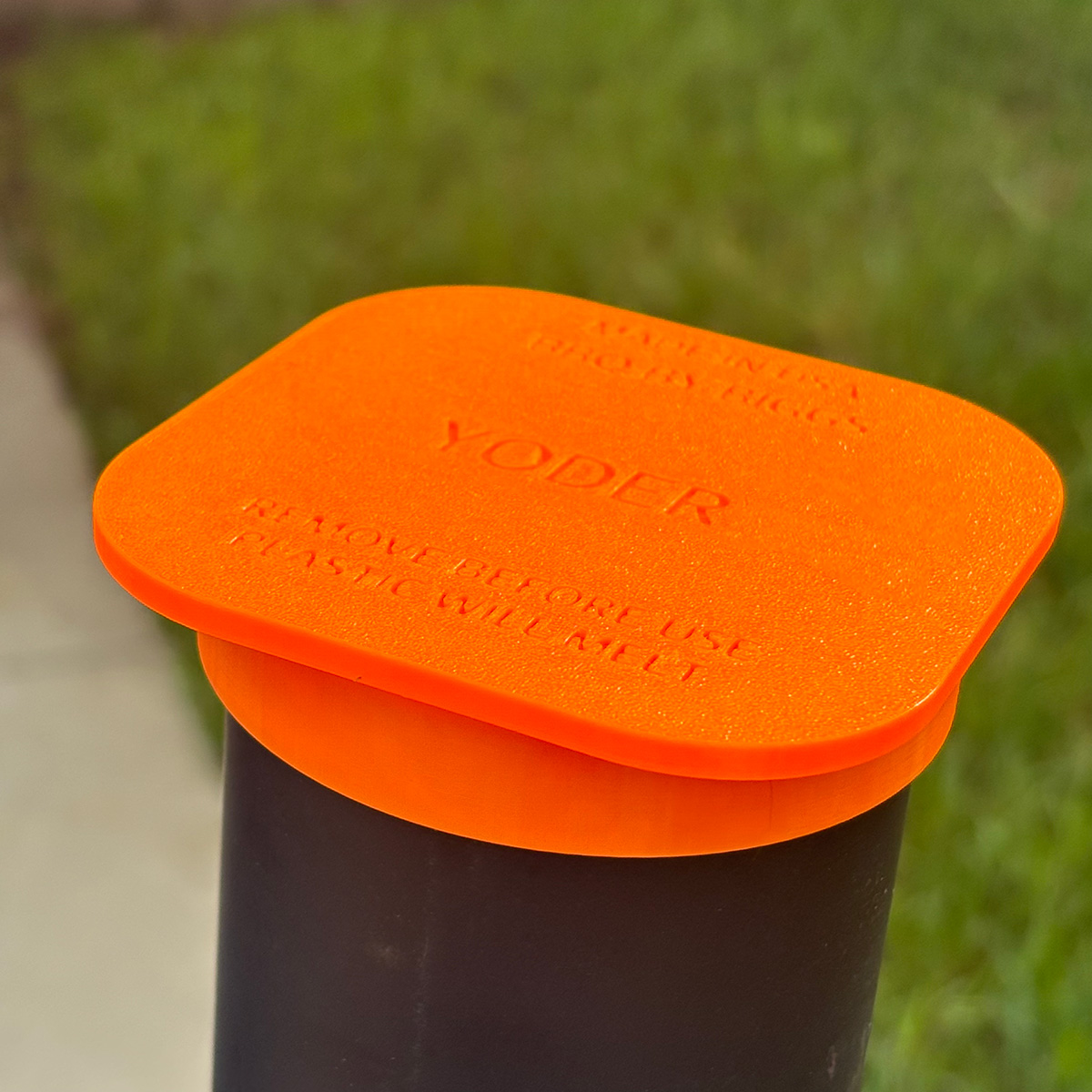 Orange lid on a black container with grass in the background yoder stack cap
